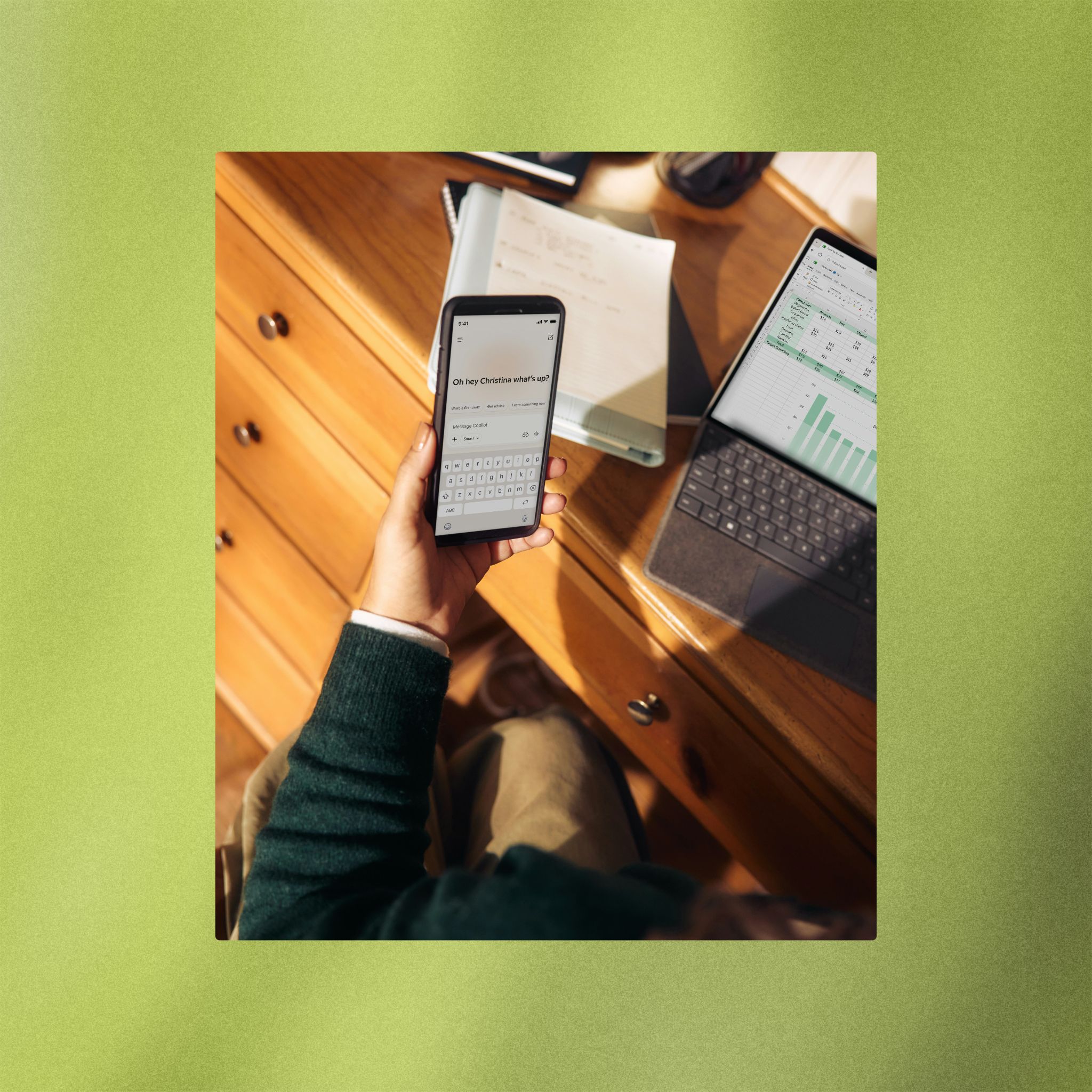 Person writing a message on a phone at a desk with a laptop
